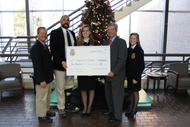 Mehrere Personen, die Zertifikate halten, mit einem Weihnachtsbaum, einer Treppe, einem Sofa, einem Tisch, einem Glas und Bäumen im Hintergrund.