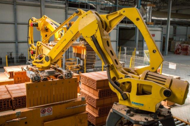 Ein großes Lager mit zahlreichen Kisten, Kränen und diverser industrieller Ausrüstung, mit einem Zaun und Pfählen im Vordergrund und einer Wand im Hintergrund.