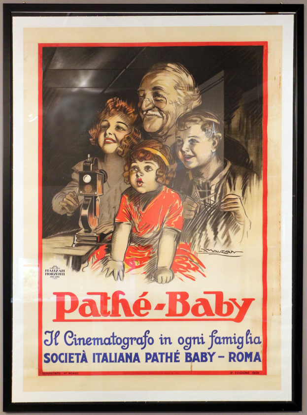 Ein Foto rahmte auf dem Wand ein Plakat einer Familie mit drei Personen mit der Aufschrift "Pathé-Baby - Il Cinematografico in Ogni Famiglia Società Italiana Pathé Baby - Roma."