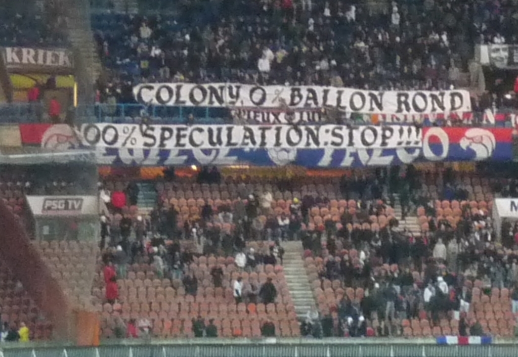 Ein Stadion voller Menschen, Fahnen und Stühle, mit einem Zaun unten und Treppen links.