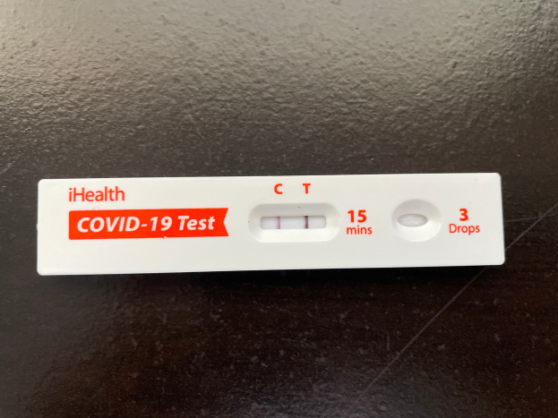 Ein wei├čer und roter Covid-19-Testthermometer mit Text und Zahlen darauf, auf einer schwarzen Oberfl├Ąche plaziert.