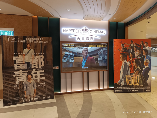 Eintritt zu den Kaiser-Kinos in Hong Kong mit Bannern, einem Bildschirm, einer Namensplatte, Deckenleuchten und einem Wasserzeichen.