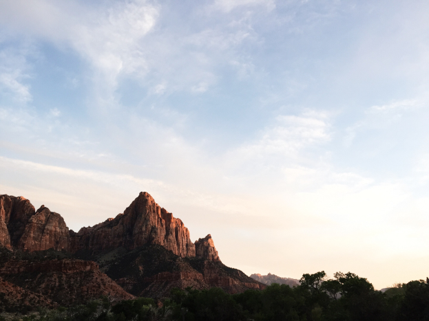Ein atemberaubender Blick auf den Zion-Nationalpark in Utah mit Bäumen, Hügeln und einem von der untergehenden Sonne erleuchteten Himmel.