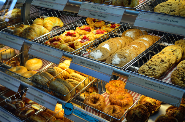 Eine Bäckereivitrine voller verschiedener Gebäcke, Torten, Kekse und anderer Backwaren, mit Schildern, die die Art der Backwaren angeben.