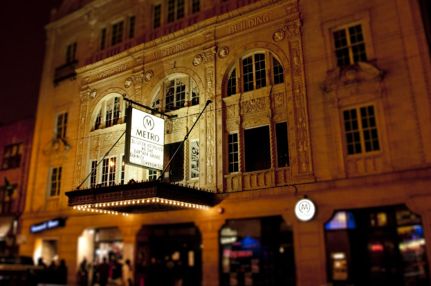 Ein gelbes Gebäude im Vordergrund mit Geschäften und einem weißen "Metro"-Schild an der unteren Vorderseite.