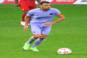 Ein Fußballspieler in Sportbekleidung und -schuhen ist im Einsatz auf dem Feld, mit einer Tafel mit Text im Hintergrund.