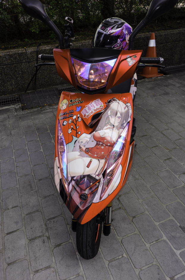 Oranger Scooter auf der Straße geparkt mit einem Helm daneben, neben einer Verkehrsinsel, einer Wand und Bäumen im Hintergrund.